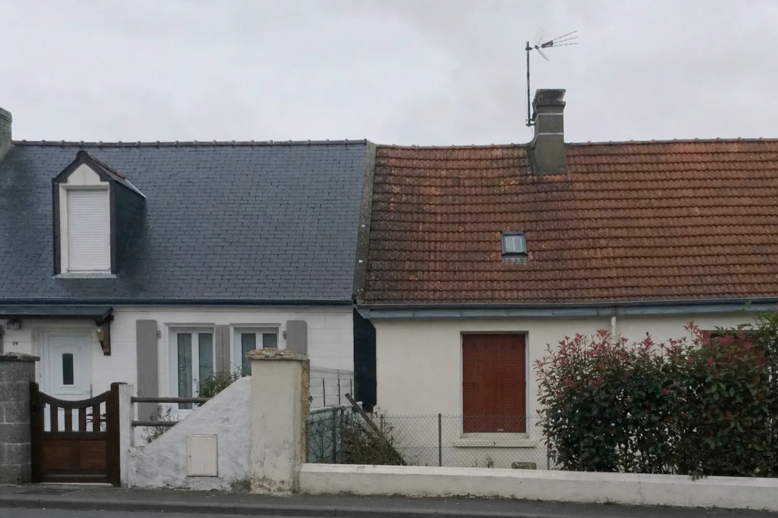 Deux toitures mitoyennes de maisons anciennes, l’une couverte d’ardoise naturelle grise, l’autre de tuile terre cuite, vues depuis la rue
