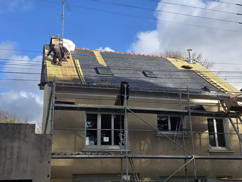 Chantier de rénovation : échafaudage monté et ardoise neuve en cours de pose